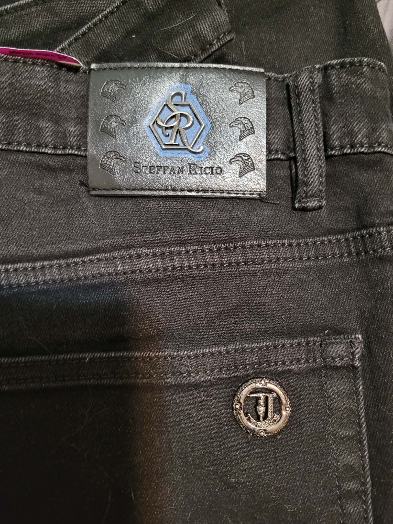 Designer denim garment with Steffan Riccio label and decorative metal emblem