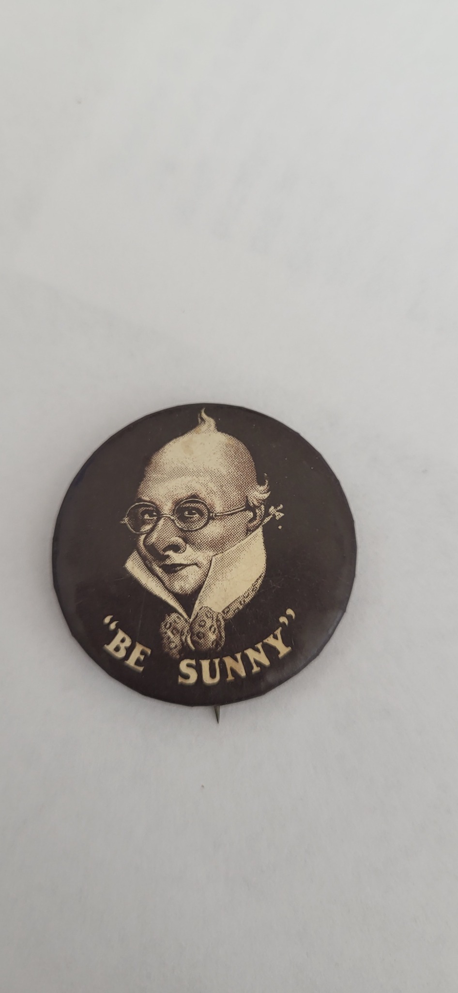 Vintage novelty pinback button or lapel pin featuring a caricature portrait and the slogan "Be Sunny"