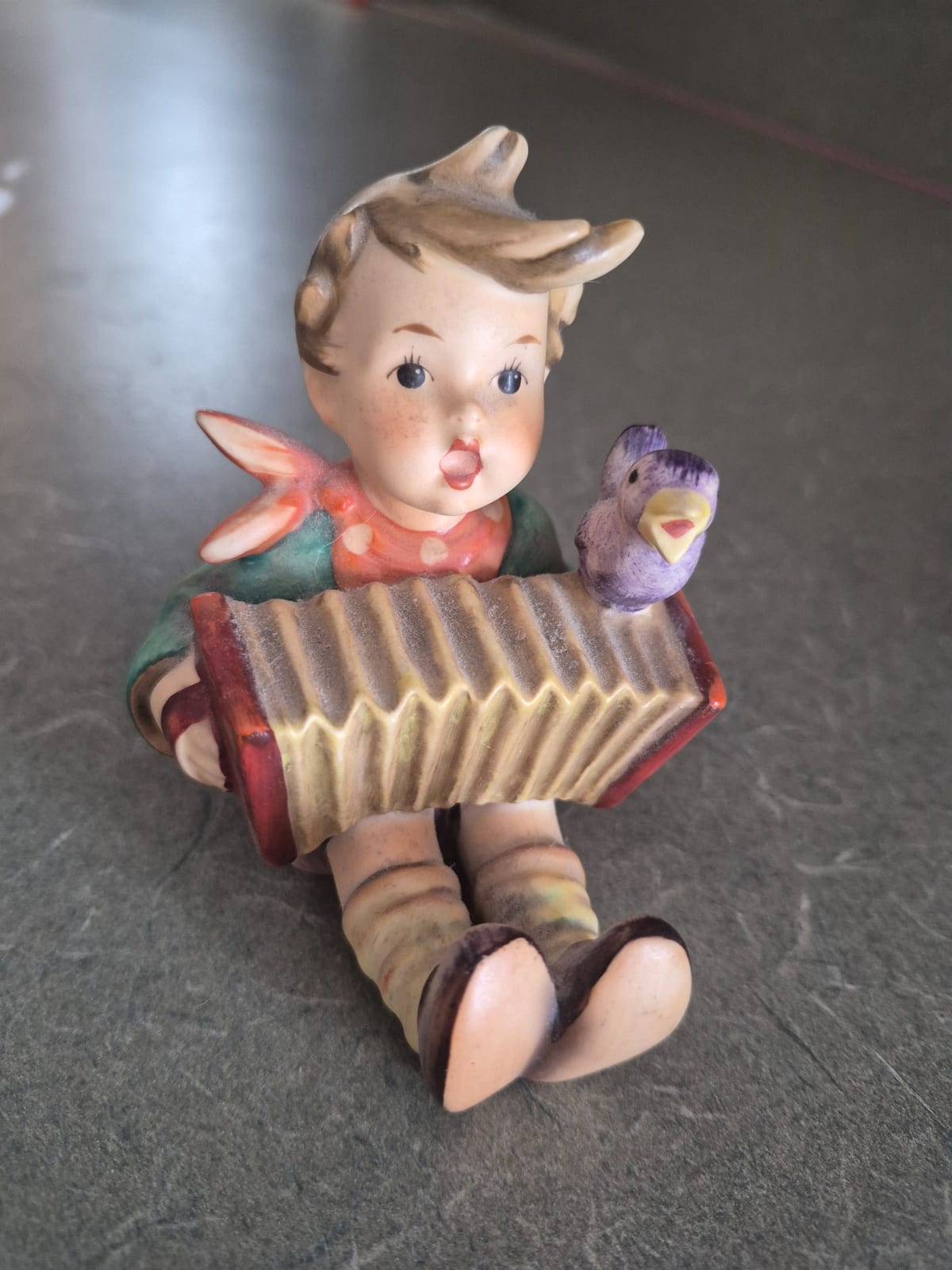 Hummel-style porcelain figurine of a child playing an accordion with bird