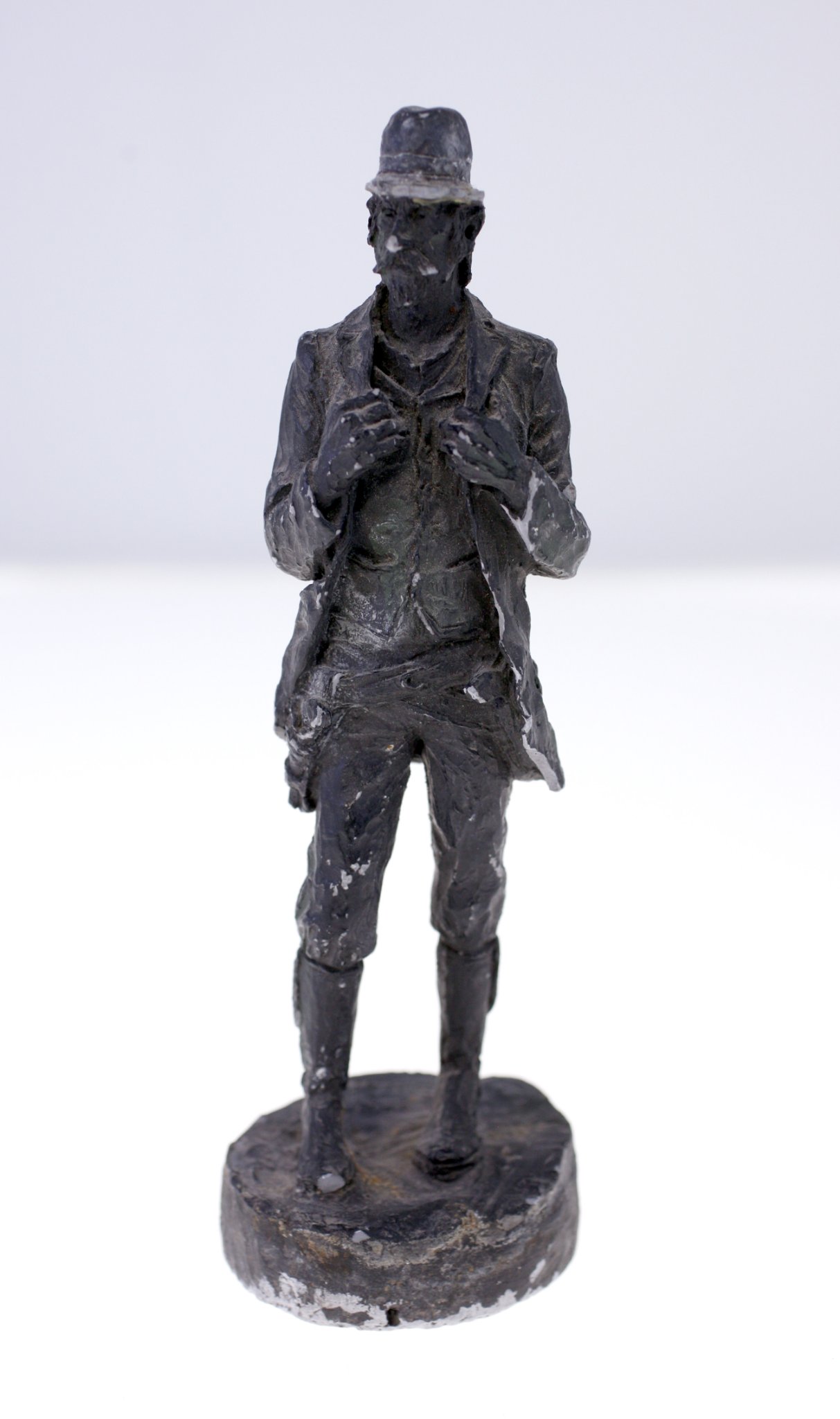 Small cast figurative sculpture of a standing man in hat and coat